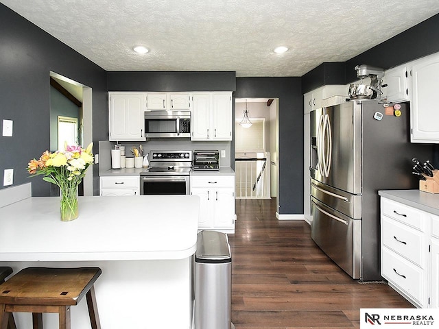 kitchen featuring stainless steel appliances, a textured ceiling, dark wood finished floors, white cabinets, and a kitchen bar