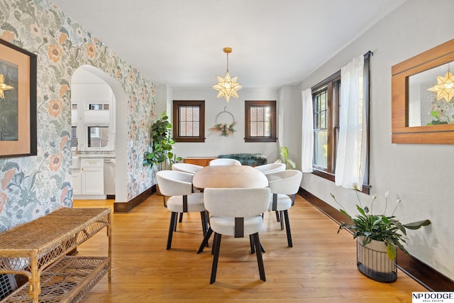 dining room with baseboards, light wood-style floors, and arched walkways