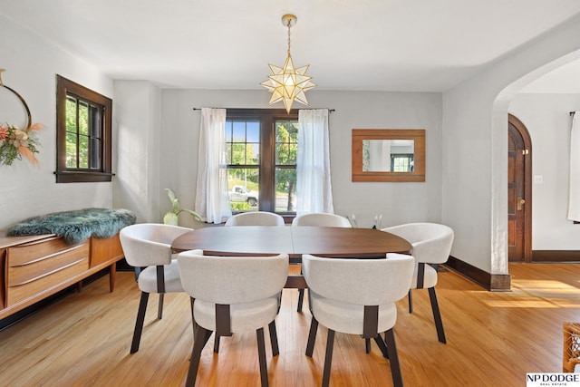 dining space with arched walkways, light wood-style flooring, and baseboards