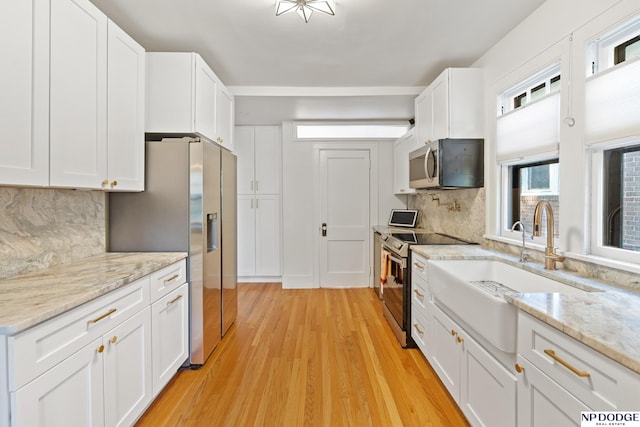 kitchen featuring stainless steel appliances, a sink, white cabinets, light wood finished floors, and decorative backsplash