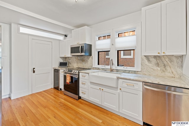 kitchen featuring appliances with stainless steel finishes, a sink, light wood-type flooring, backsplash, and white cabinets