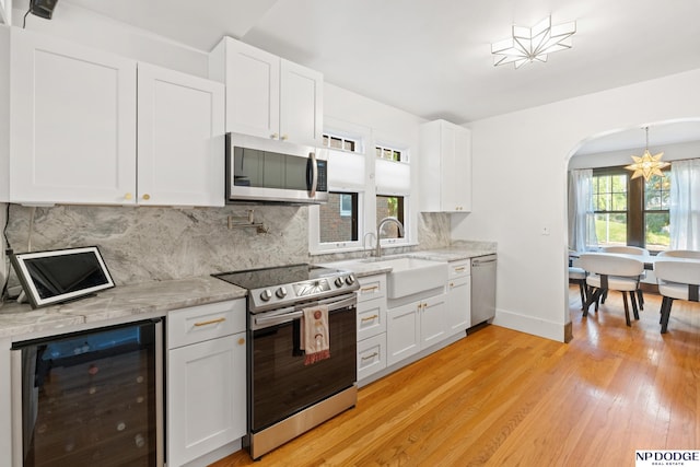 kitchen with wine cooler, stainless steel appliances, a sink, backsplash, and white cabinets