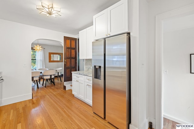kitchen featuring stainless steel fridge, arched walkways, white cabinetry, light wood-style floors, and baseboards