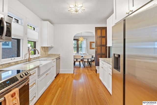 kitchen featuring appliances with stainless steel finishes, arched walkways, light wood-style floors, a sink, and white cabinetry