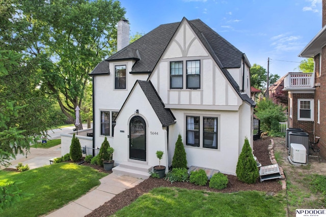english style home featuring stucco siding, roof with shingles, and a chimney