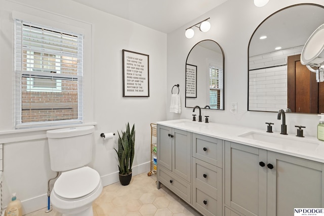 bathroom with healthy amount of natural light, toilet, double vanity, baseboards, and recessed lighting