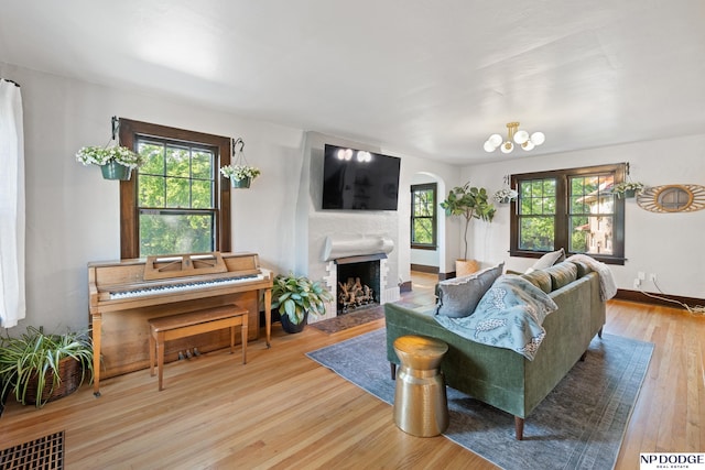 living room with arched walkways, wood finished floors, plenty of natural light, and a fireplace with raised hearth