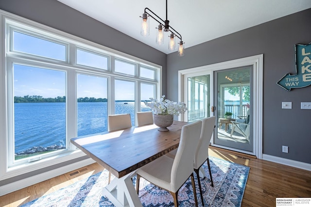 dining area with baseboards, a water view, and wood finished floors