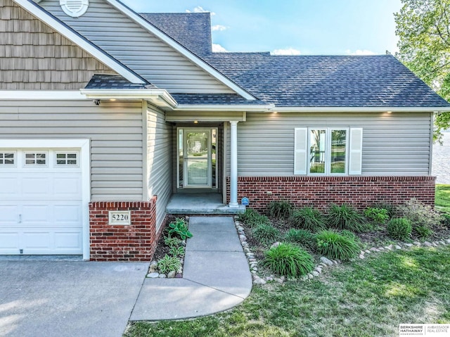 view of exterior entry featuring an attached garage, brick siding, and a shingled roof