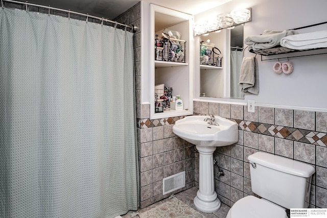 full bathroom with tile walls, toilet, wainscoting, and tile patterned floors