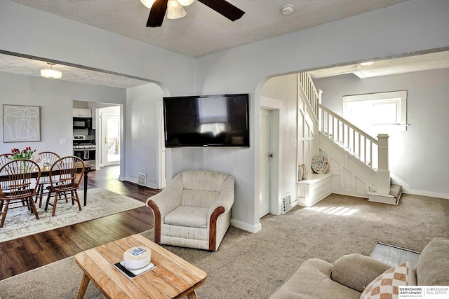 living room featuring ceiling fan, stairs, a textured ceiling, baseboards, and arched walkways