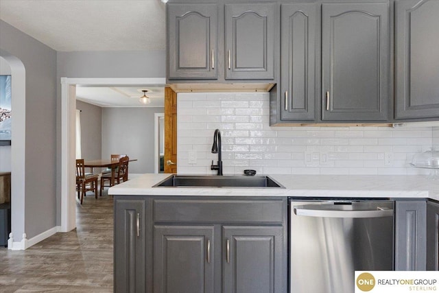 kitchen with stainless steel dishwasher, a sink, gray cabinets, and tasteful backsplash