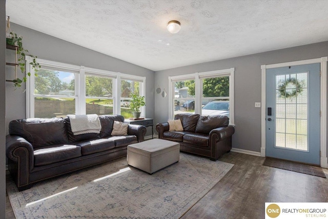 living area with wood finished floors, vaulted ceiling, a textured ceiling, and baseboards