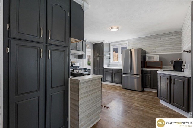 kitchen featuring stainless steel appliances, under cabinet range hood, light countertops, and dark wood-style flooring
