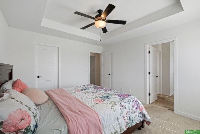 bedroom with a raised ceiling, light carpet, baseboards, and a ceiling fan