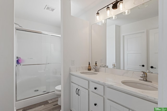 bathroom with toilet, a shower stall, double vanity, and wood finished floors