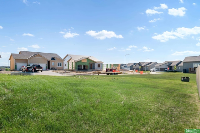 view of green lawn featuring a residential view, an attached garage, and driveway