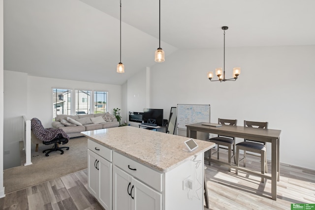 kitchen with light wood-type flooring, lofted ceiling, a kitchen island, a chandelier, and white cabinets