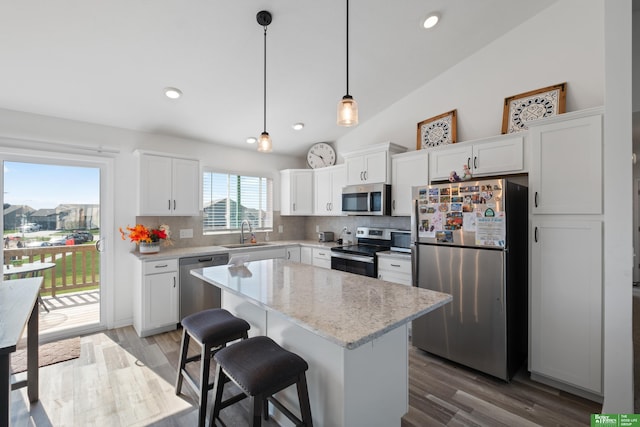 kitchen featuring stainless steel appliances, a sink, tasteful backsplash, lofted ceiling, and white cabinetry