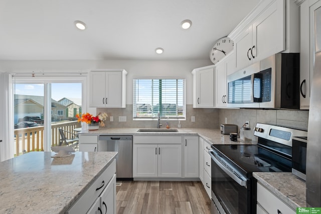 kitchen with stainless steel appliances, a sink, light wood-type flooring, white cabinets, and decorative backsplash
