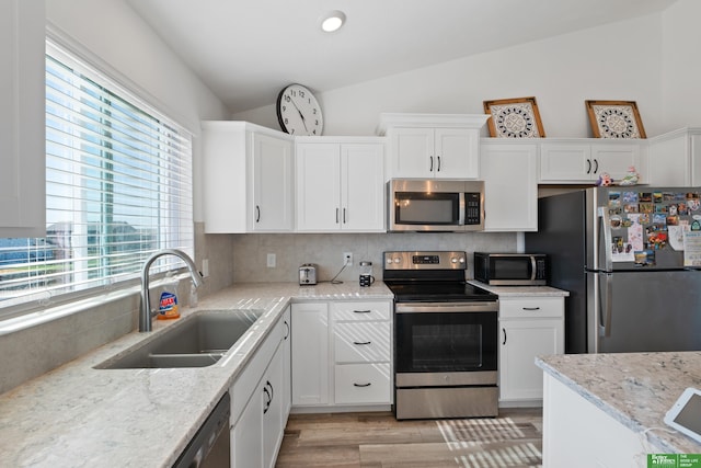 kitchen featuring stainless steel appliances, a sink, vaulted ceiling, backsplash, and white cabinets