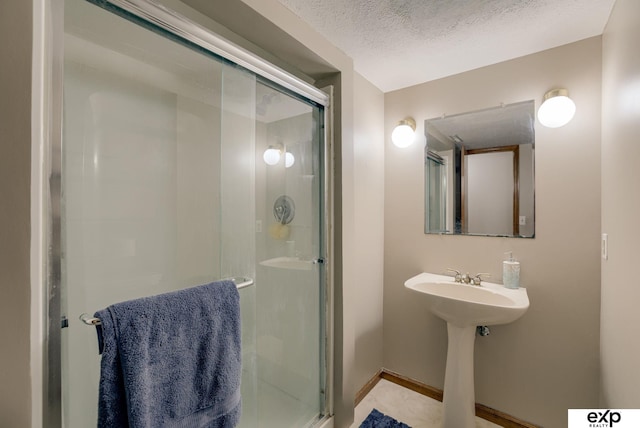 full bath featuring a stall shower, a textured ceiling, and baseboards