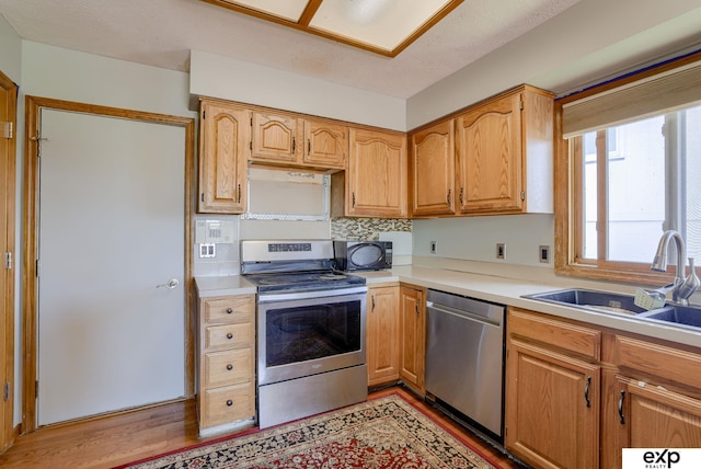 kitchen featuring stainless steel appliances, a sink, light countertops, light wood finished floors, and tasteful backsplash