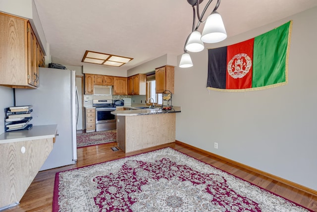 kitchen featuring appliances with stainless steel finishes, a sink, light wood-style flooring, and a peninsula