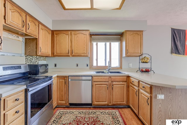 kitchen with appliances with stainless steel finishes, a sink, a peninsula, light countertops, and light wood finished floors