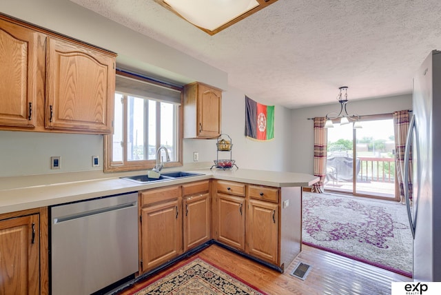 kitchen featuring stainless steel appliances, plenty of natural light, a peninsula, a textured ceiling, and a sink