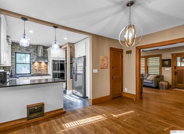 1530 S 52nd St, Omaha, NE 68106 - kitchen with wall chimney exhaust hood, appliances with stainless steel finishes, dark countertops, white cabinetry, and a chandelier