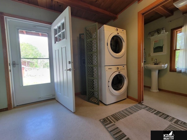 clothes washing area featuring stacked washer / drying machine, healthy amount of natural light, wooden ceiling, and baseboards