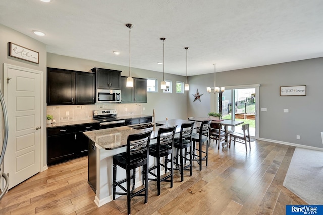 7308 Andy Dr, Lincoln, NE 68516 - kitchen featuring appliances with stainless steel finishes, a sink, a kitchen island with sink, light wood-style flooring, and a breakfast bar area