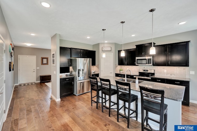 7308 Andy Dr, Lincoln, NE 68516 - kitchen with stainless steel appliances, dark cabinets, a sink, a breakfast bar, and light wood-type flooring