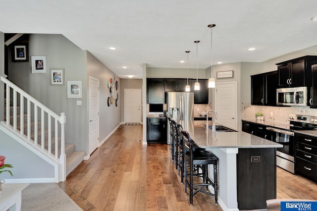 7308 Andy Dr, Lincoln, NE 68516 - kitchen featuring appliances with stainless steel finishes, a sink, a breakfast bar area, dark cabinetry, and light stone counters