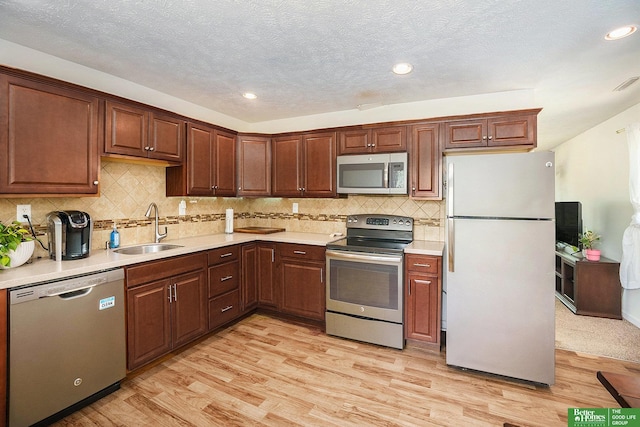 kitchen featuring stainless steel appliances, a sink, light wood-type flooring, light countertops, and recessed lighting