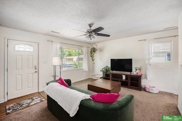 carpeted living room featuring a ceiling fan, baseboards, and a textured ceiling
