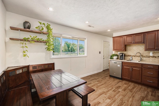 kitchen featuring dishwasher, a sink, light countertops, tasteful backsplash, and light wood-style flooring