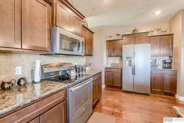 8902 N 161st Ave, Bennington, NE 68007 - kitchen featuring appliances with stainless steel finishes, light wood-style flooring, decorative backsplash, stone counters, and a textured ceiling