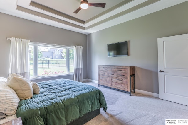 carpeted bedroom with a raised ceiling, baseboards, and ceiling fan