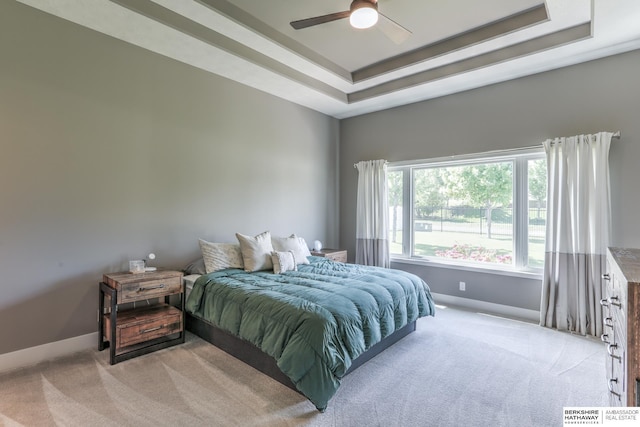 bedroom with light colored carpet, baseboards, a tray ceiling, and ceiling fan