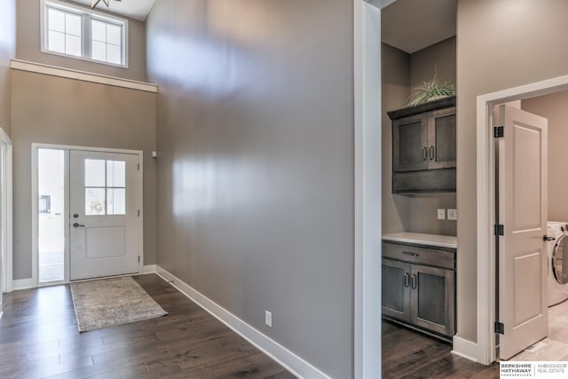 entryway with washer / clothes dryer, dark wood-type flooring, baseboards, and a high ceiling