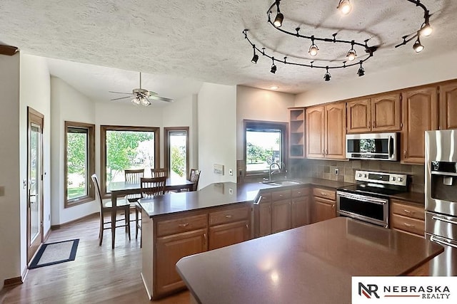 kitchen with stainless steel appliances, a sink, dark countertops, decorative backsplash, and a peninsula