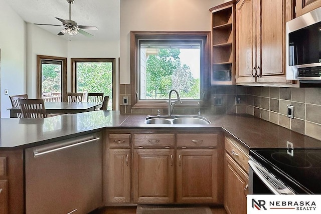 kitchen with appliances with stainless steel finishes, a sink, ceiling fan, a peninsula, and backsplash