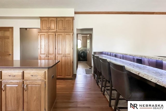 kitchen featuring dark wood-style flooring, crown molding, washer / clothes dryer, and brown cabinets