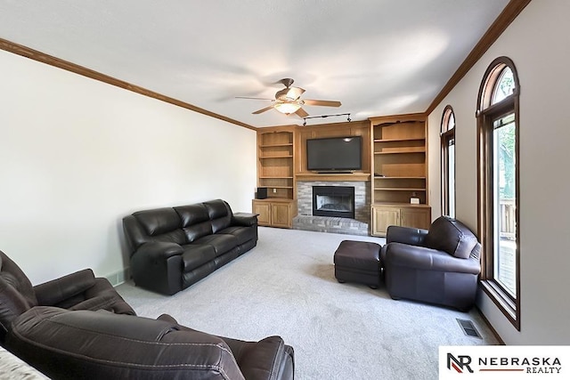living area with crown molding, carpet floors, a ceiling fan, a stone fireplace, and baseboards