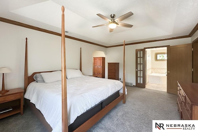bedroom with a tray ceiling, light carpet, crown molding, connected bathroom, and ceiling fan