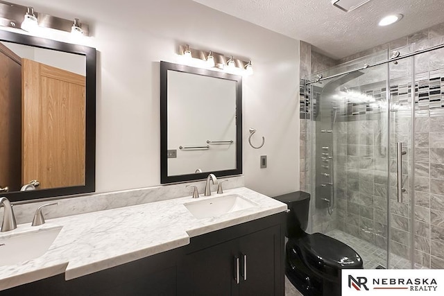 full bathroom featuring a shower stall, double vanity, a textured ceiling, and toilet