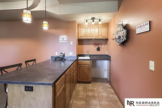 kitchen featuring a peninsula, dark countertops, a sink, light tile patterned floors, and a breakfast bar