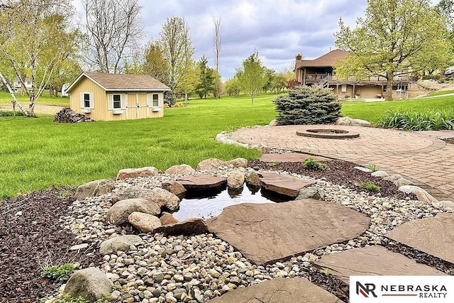 view of grassy yard with an outdoor fire pit, an outbuilding, and a patio